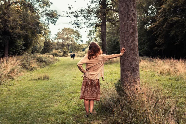 Ung kvinna lesaning mot ett träd i skogen — Stockfoto