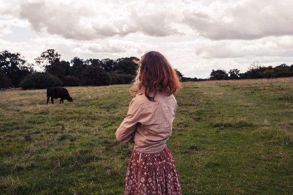 Young woman standing in field with cows — Stock Photo, Image