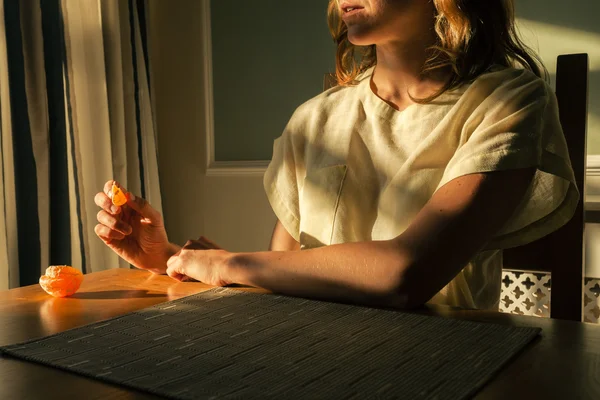 Jonge vrouw zitten aan tafel met een oranje — Stockfoto