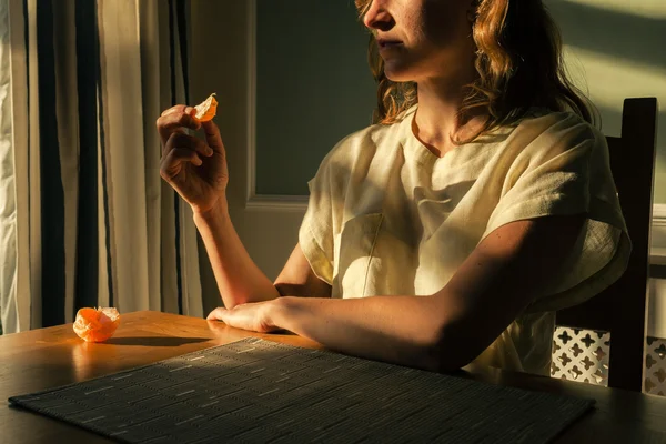 Mladá žena, sedící u stolu s oranžová — Stock fotografie