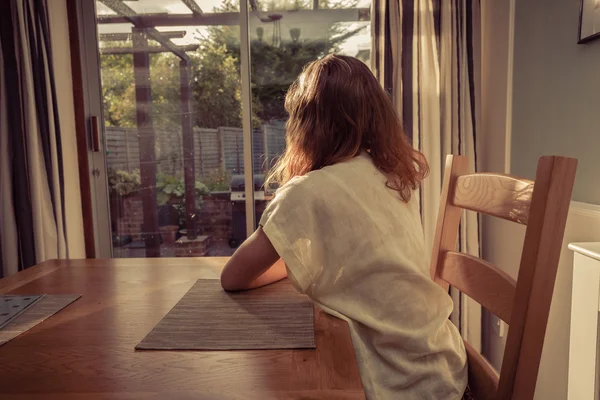 Молодая женщина сидит за столом и смотрит в окно — стоковое фото