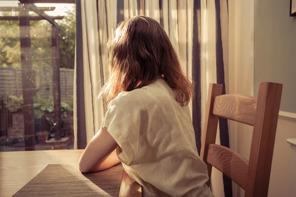 Mladá žena sedí u stolu a díval se z okna — Stock fotografie