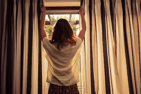 Ung kvinna öppna gardiner på sunrise — Stockfoto