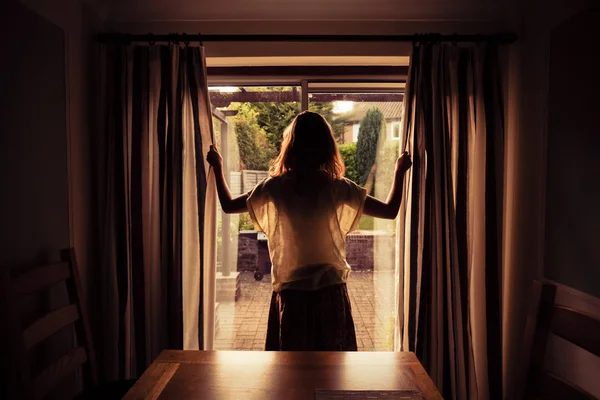 Mujer joven abriendo las cortinas al amanecer —  Fotos de Stock