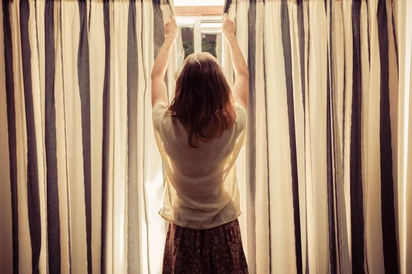 Mujer joven abriendo las cortinas al amanecer —  Fotos de Stock