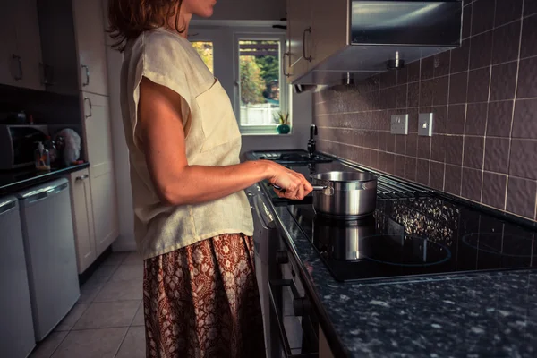 Young woman in kitchen cooking with saucepan — Stock Photo, Image