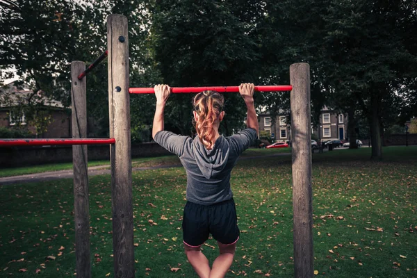 Jonge vrouw doen pullups in het park — Stockfoto