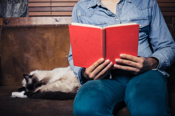 Man die leest op sofa met kat — Stockfoto