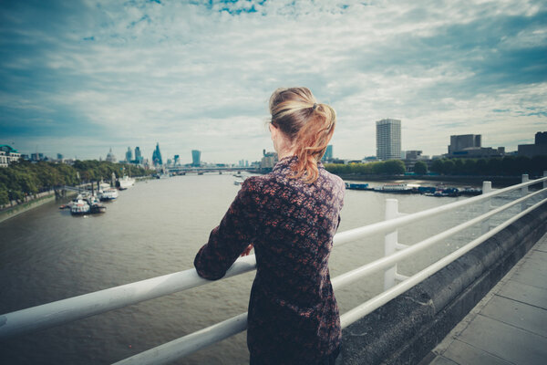 A young woman is standing on a bridge in the city and is admiring the skyline