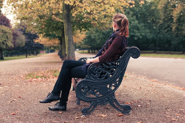 Jovem mulher sentada no banco do parque — Fotografia de Stock