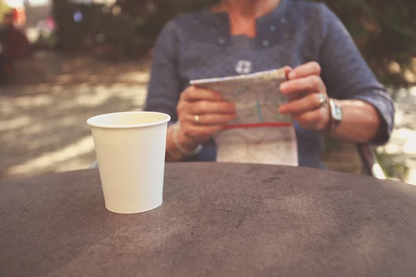 Elderly woman studying map and having coffee — Stock Photo, Image