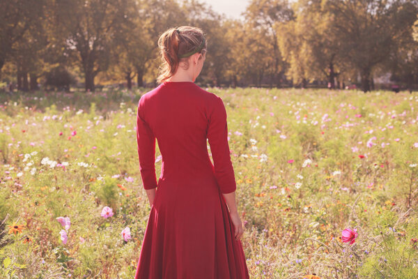 A young woman wearing a red dress is standing in a meadow at sunset