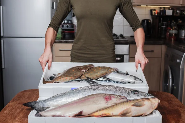 Vrouw met een doos van vis in haar keuken — Stockfoto