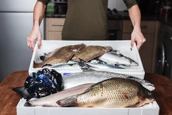 Mulher com uma caixa de peixe em sua cozinha — Fotografia de Stock