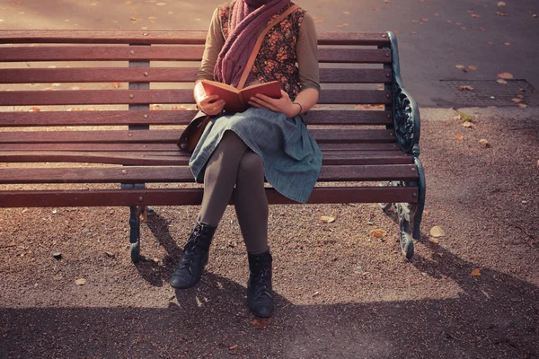 Young woman sitting on park bench with book — Stock Photo, Image