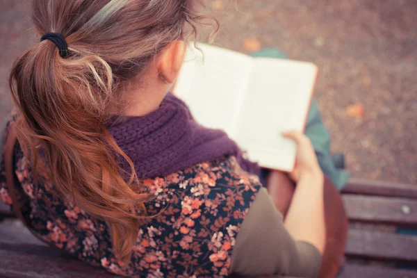 Jovem mulher sentada no banco do parque com livro — Fotografia de Stock