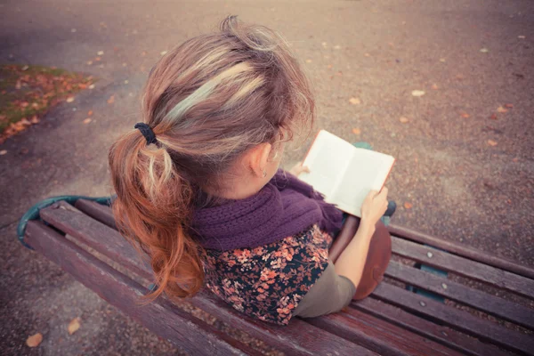 Young woman sitting on park bench with book — Stock Photo, Image
