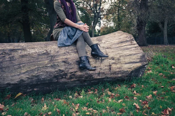 Woman sitting on a fallen tree in the park — Stock Photo, Image