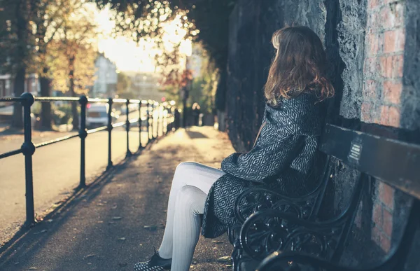 Jeune femme assise sur le banc au coucher du soleil — Photo