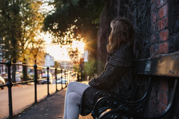 Jovem mulher sentada no banco ao pôr do sol — Fotografia de Stock