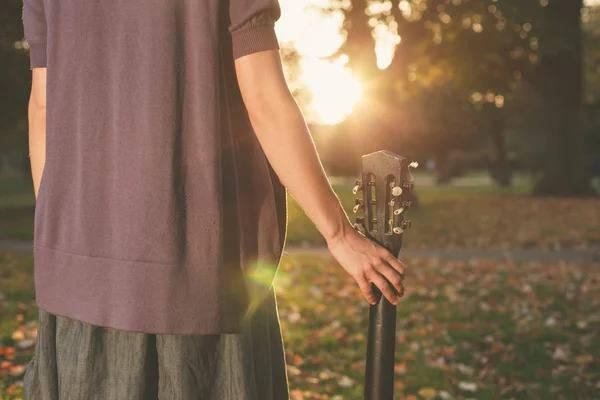 Kvinna med gitarr vid solnedgången i park — Stockfoto