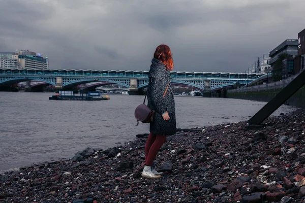 Ung kvinna stående på flodstranden i city — Stockfoto