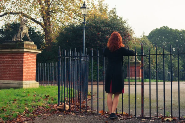 Mujer apoyada en la puerta del parque — Foto de Stock