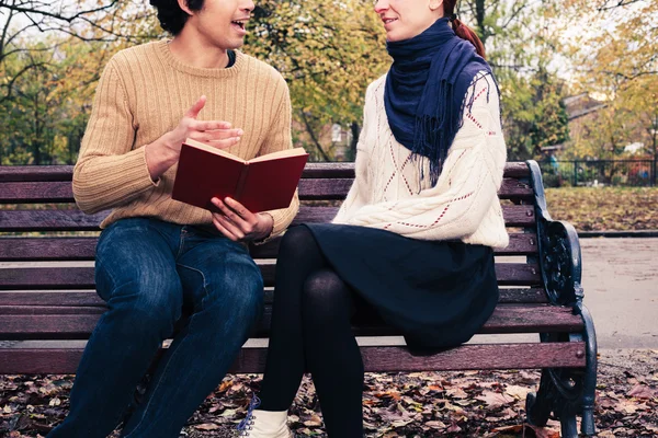 Мужчина читает для женщины на скамейке в парке — стоковое фото