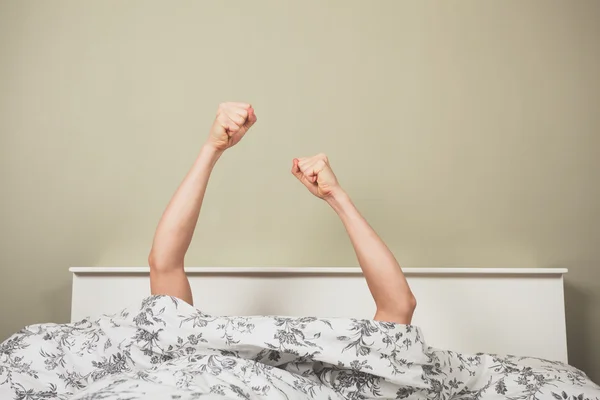 Woman raising her fists from under the covers — Stock Photo, Image