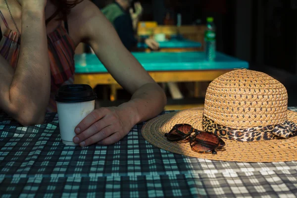 Young woman sitting at table with a hat — Stock Photo, Image