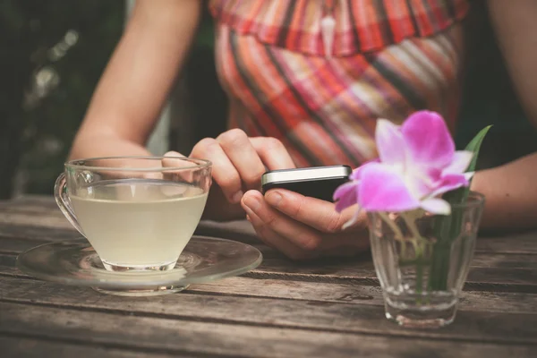 Giovane donna che beve tè e utilizza il suo telefono — Foto Stock