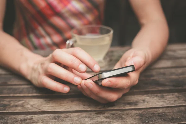 Jonge vrouw drinken thee en het gebruik van haar telefoon — Stockfoto