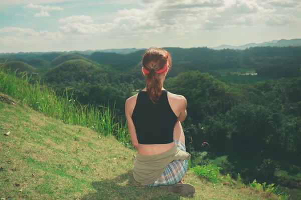 Jovem mulher sentada em uma colina e admirando vista — Fotografia de Stock