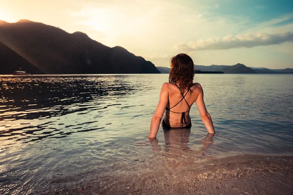 Young woman in swimsuit sitting on tropical beach — Stock Photo, Image