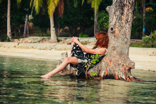 Woman sitting up against tree on tropical beach — Stock Photo, Image