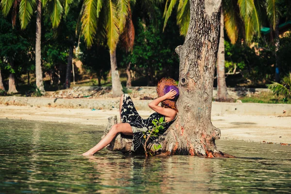 Woman sitting up against tree on tropical beach — Stock Photo, Image