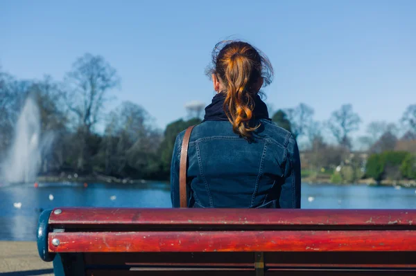 Woman sitting on bench by pond — Stock Photo, Image