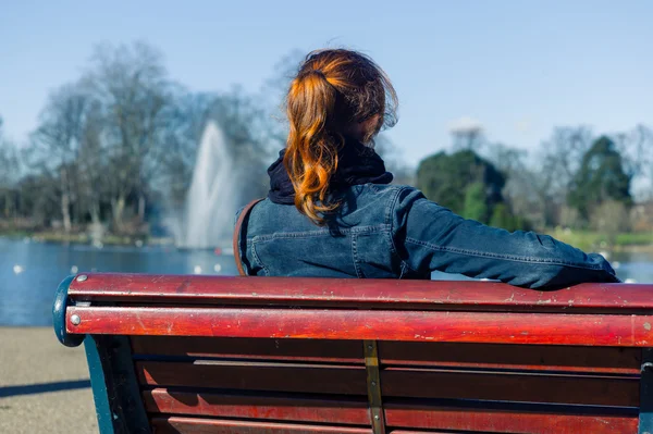 Woman sitting on bench by pond — Stock Photo, Image