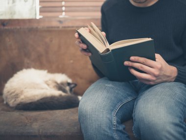 Kedi ile kanepede oturan genç adam okuyor