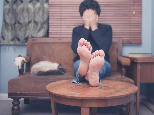 Barefoot man sitting on sofa and covering his face — Stock Photo, Image