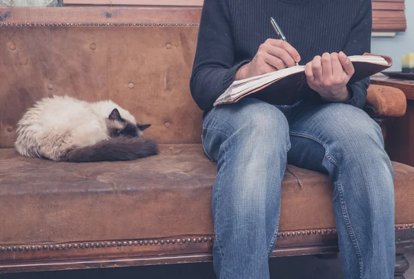 Mann sitzt auf Sofa und schreibt Notizbuch — Stockfoto