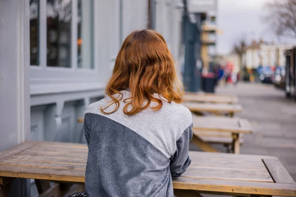 Young woman sitting on bench outside pub — Stock Photo, Image
