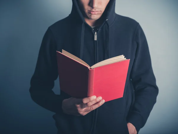 Young man in hooded top reading red book — Stock Photo, Image