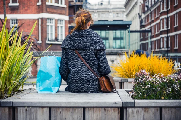 Jeune femme avec des achats reposant sur le banc — Photo