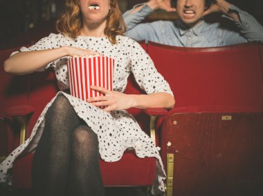 Woman annoying man in cinema by eating popcorn clipart