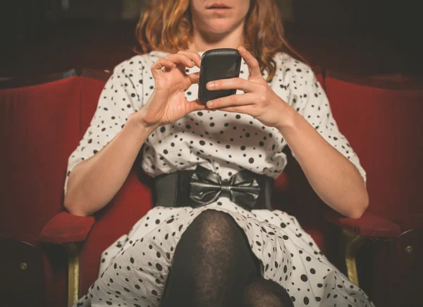 Młoda kobieta w pierwszym rzędzie kino za pomocą jej telefon — Zdjęcie stockowe