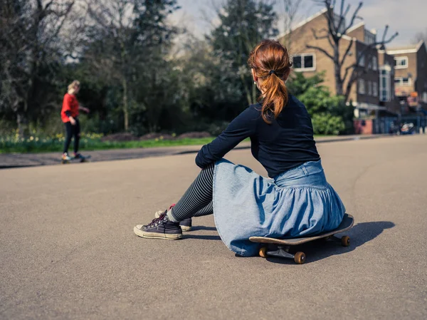 Woman sitting on skateboard in the park — Stock Photo, Image