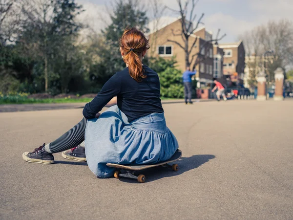 Женщина сидит на скейтборде в парке — стоковое фото