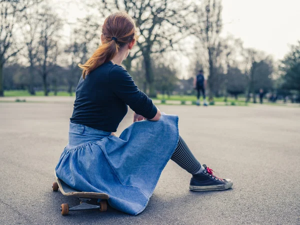 Woman sitting on a skateboard in the park — Stock Photo, Image