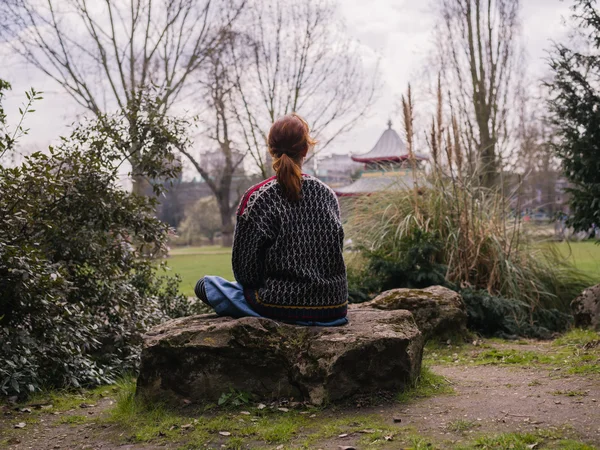 Jovem mulher sentada em uma rocha no parque — Fotografia de Stock